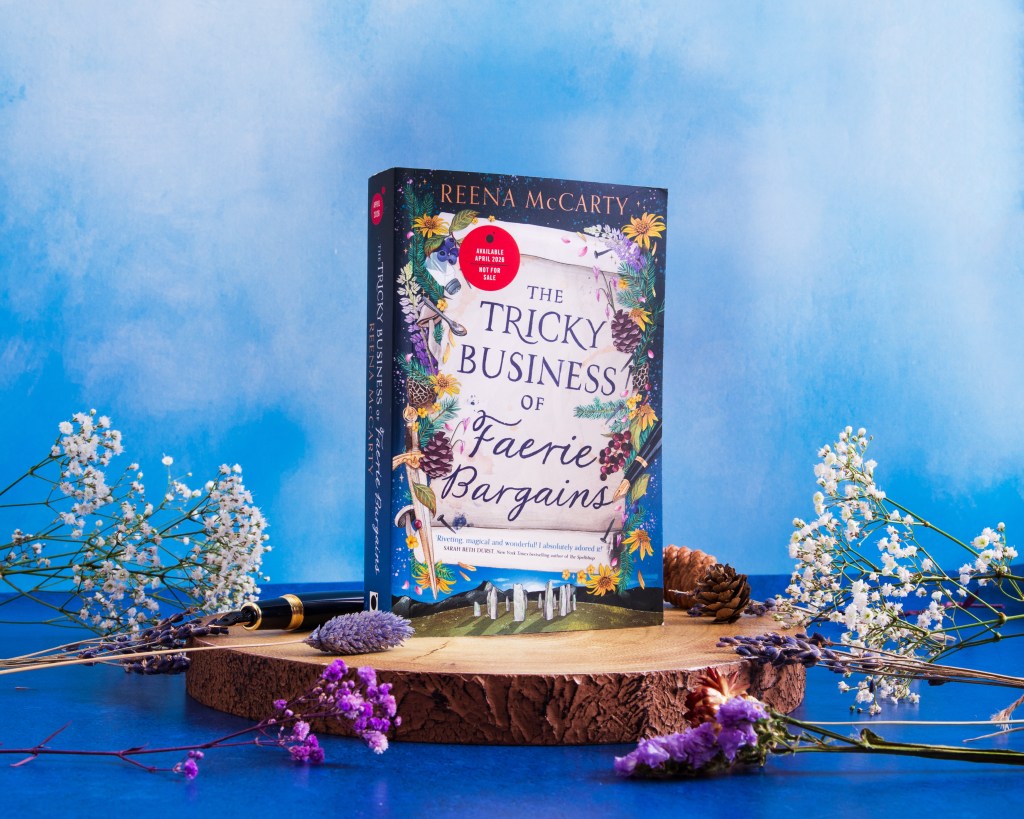 The Tricky Business of Faerie Bargains book on wooden log with flowers surrounding it