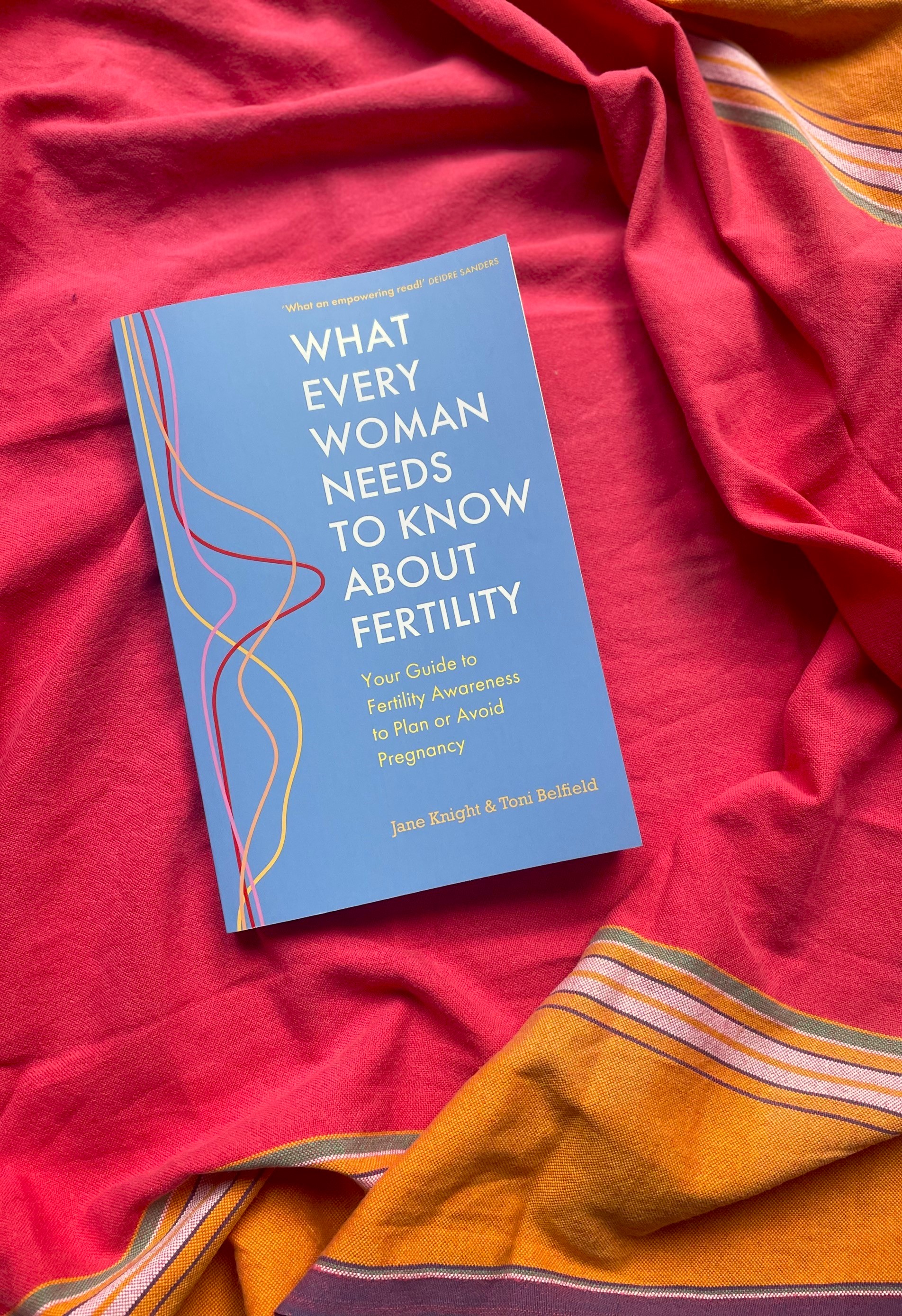 A photograph of the book What Every Woman Needs to Know About Fertility placed on a red fabric background.