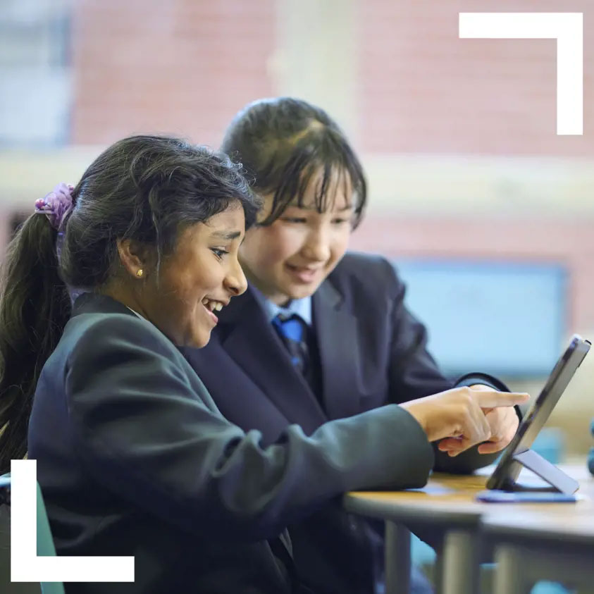 Two key stage 3 pupils scrolling on a tablet and smiling